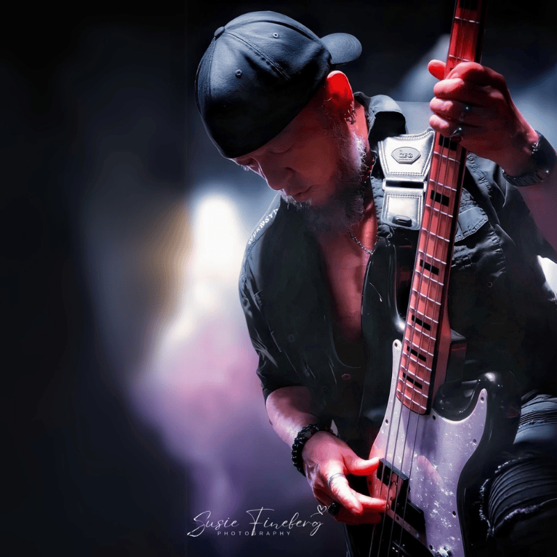 Scott Rippons performing live with a bass guitar, using the CFG (Cable-Free Guitar) Zero Gravity strap for enhanced comfort and mobility. The image captures an intense stage moment with dramatic lighting, highlighting the strap's ergonomic design and cable-free setup.